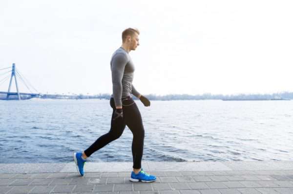 مردی با لباس ورزشکاری در حال پیاده‌روی کنار دریا با هدفون در گوش