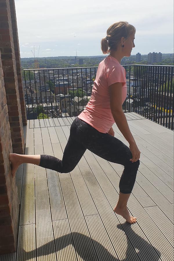 ورزشکار در حال انجام لانج دیواری با بلندکردن پاشنه برای درمان مصدومیت کشیدگی عضلانی ساق در دونده‌ها 