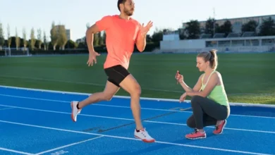 دونده آقا در حال دویدن روی پیست در کنار خانم مربی با کرنومتر در دست برای ثبت زمان دویدن دونده مرد