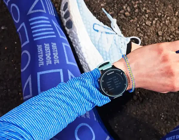 دونده نشسته روی زمین در حال تماشای ساعت هوشمند خود