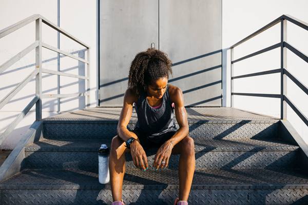 دونده خانم نشسته روی پله و خسته از نظر روانی در کنار بطری آب